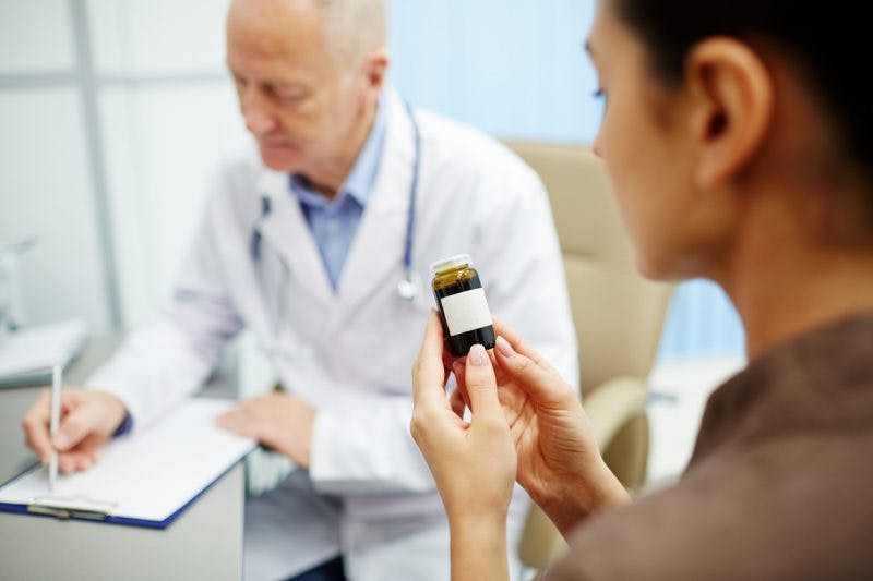 woman reading label of bottle of aricept for brain injury while doctor writes instructions in the background
