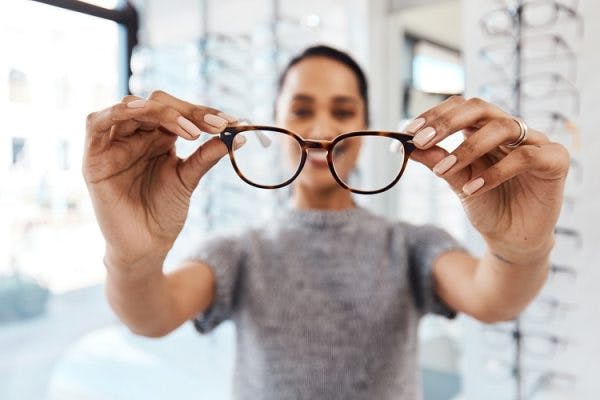 woman holding out a pair of glasses to help with blurred vision in one eye after head injury
