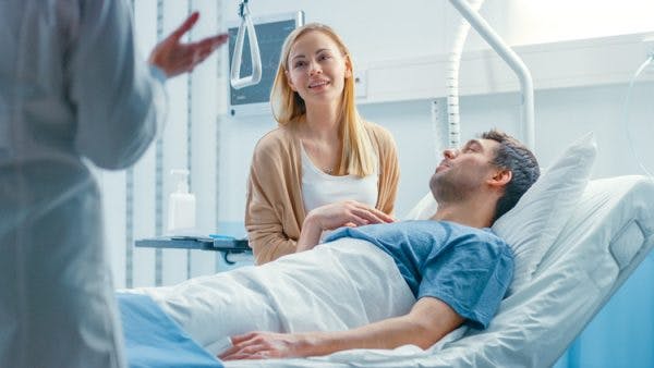 Doctor standing at foot of hospital explaining brain injury recovery statistics to patient and his wife
