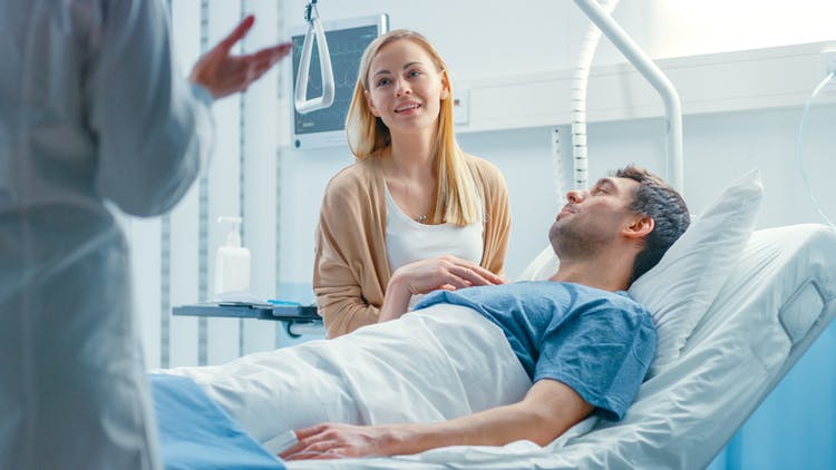 Doctor standing at foot of hospital explaining brain injury recovery statistics to patient and his wife