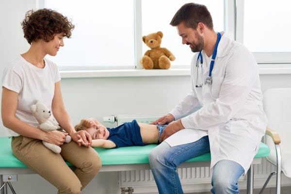 Pediatrician palpating stomach of little child with cerebral palsy who has been vomiting