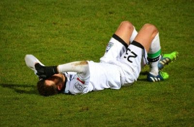 soccer player lying on grass holding his head because he has a concussion