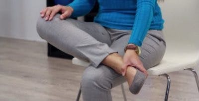 La physiothérapeute assise, les jambes croisées droite sur gauche, se pose pour vous montrer le commencement de l’exercice.