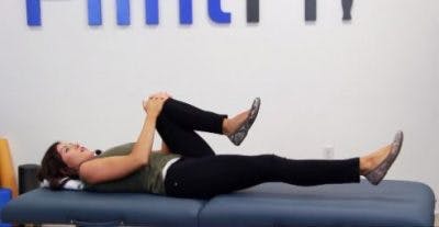 La physiothérapeute allongée tire le genou gauche à la poitrine.