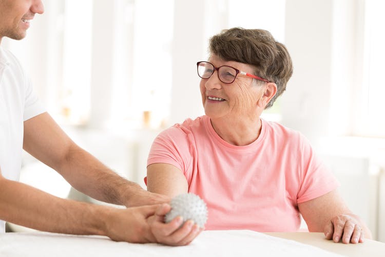 physical therapist placing hand therapy ball into stroke patients hand in clinic setting