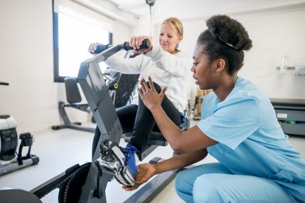 physiotherapist helping patient with hemiplegia use stationary bike