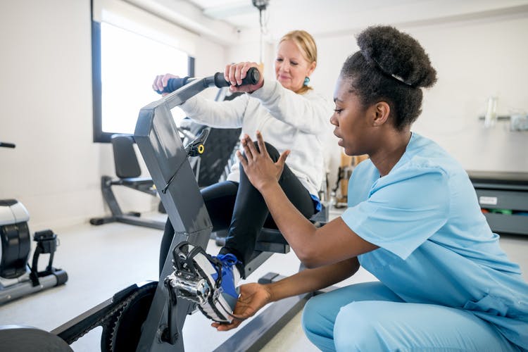 physiotherapist helping patient with hemiplegia use stationary bike
