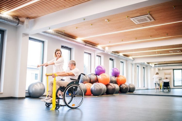 Physiotherapeut, der mit Hemiplegiepatienten in einer geräumigen Physiotherapieklinik arbeitet