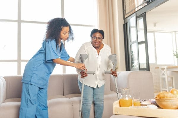 home health nurse helping stroke patient stand up from couch using cane to avoid falls