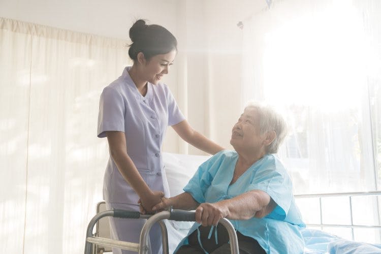 home health care workers standing next to stroke patient inside living room with hand on shoulder while stroke patient holds walker