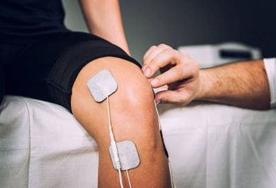Un patient essaie la stimulation électrique, assis sur un lit avec des cousinettes sur la jambe : une thérapie très utile en faisant bouger les membres affectée, en particulière quand on l'utiliser avec d'autres types de thérapie physique.