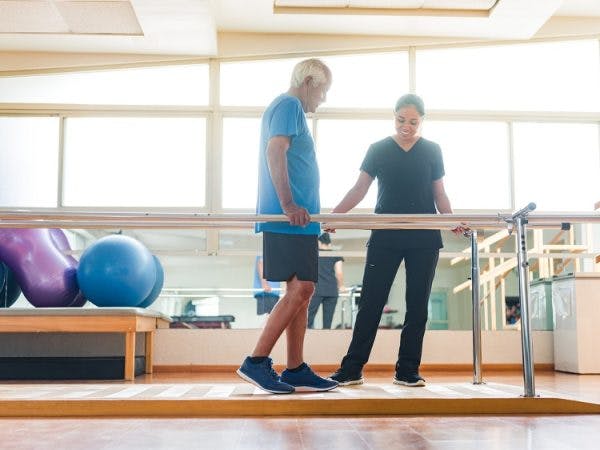 physical therapist working with man on traumatic brain injury recovery stages and relearning to walk