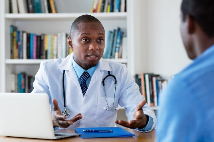Doctor sentado en un escritorio hablando con paciente de accidente cerebrovascular del lóbulo parietal acerca de la rehabilitación