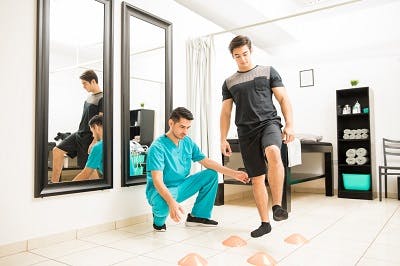 Physical therapist motivating male patient to walk between cones in hospital to promote neuroplasticity