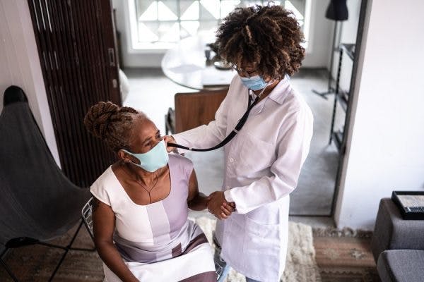 doctor visiting spinal cord injury survivor at home and using stethoscope to listen to heart beat