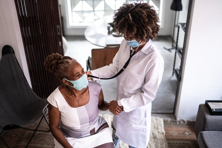doctor visiting spinal cord injury survivor at home and using stethoscope to listen to heart beat