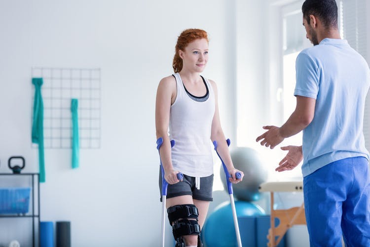 young stroke survivor with crutches participating in physiotherapy to recover her gait and ability to walk