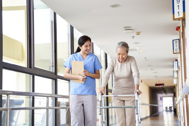 rehabilitation nurse standing next to stroke patient using a walker to recover from paralysis
