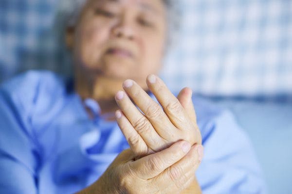 old Asian woman in hospital bed holding shaking hand after stroke