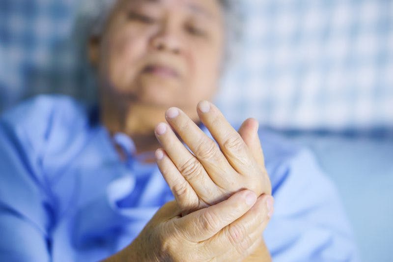 old Asian woman in hospital bed holding shaking hand after stroke