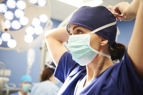 Side view of young female surgeon tying her surgical mask, discussing the types of surgery for head injury with her colleagues