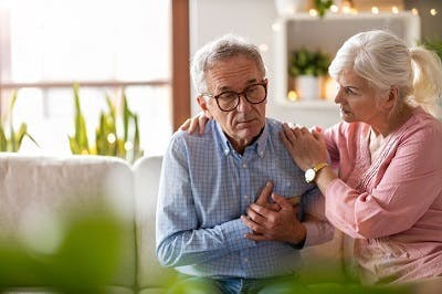 Une femme réconforte son mari qui tient les main au cœur en faisant face à une crise d'épilepsie à la suite d'un AVC.