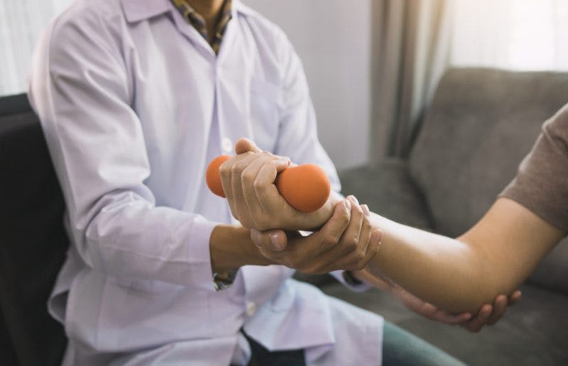 Physiotherapist helps patient raise dumbbells because he has muscle atrophy after stroke