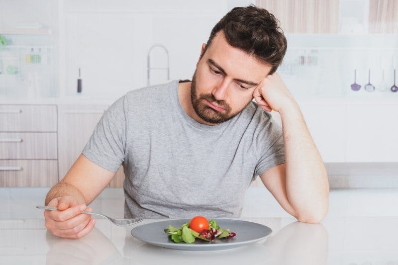 man looking at plate of food not hungry because he is fighting weight loss after brain injury