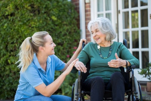 caregiver crouching near elderly transcortical sensory aphasia patient in wheelchair