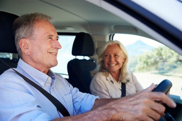 senior man driving for the first time after his stroke, his wife is in the passenger seat smiling at him
