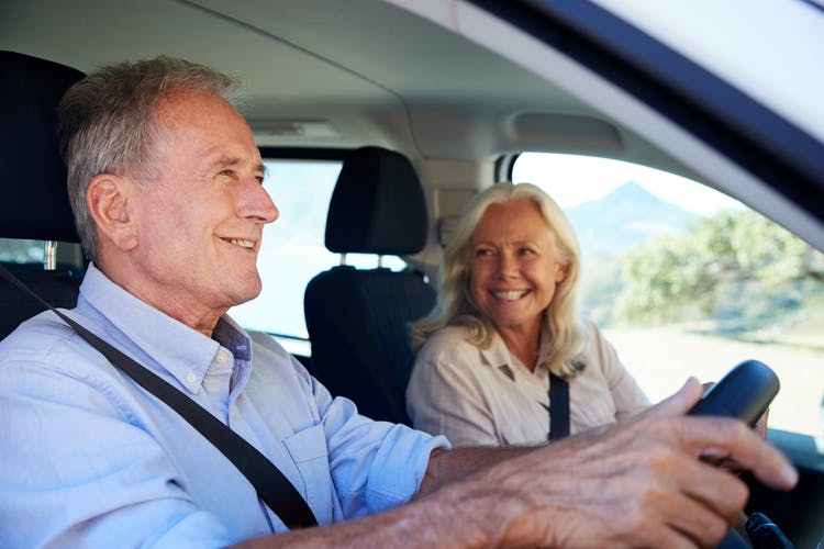 senior man driving for the first time after his stroke, his wife is in the passenger seat smiling at him