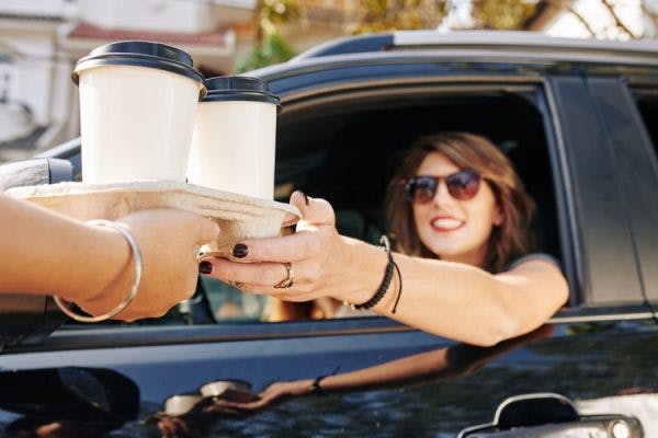 woman in car reaching for to-go coffee cups in drive-thru window because she needs caffeine after brain injury