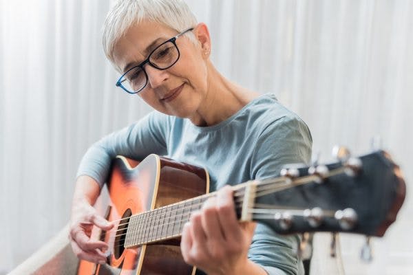 Senior woman playing guitar as part of her TBI music therapy program